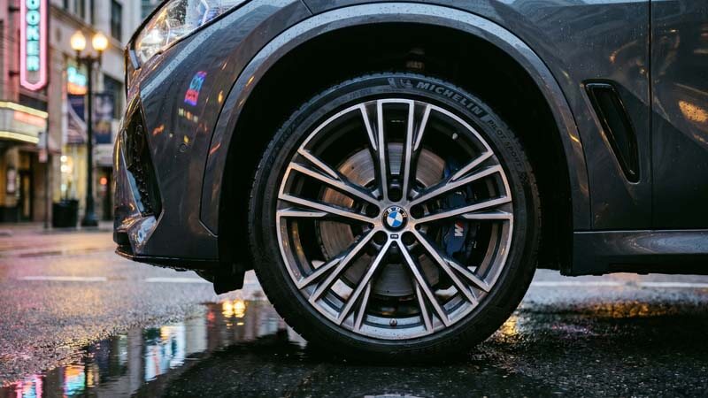 Премиальный легкосплавный диск и спортивная шина BMW на мокром асфальте с отражениями